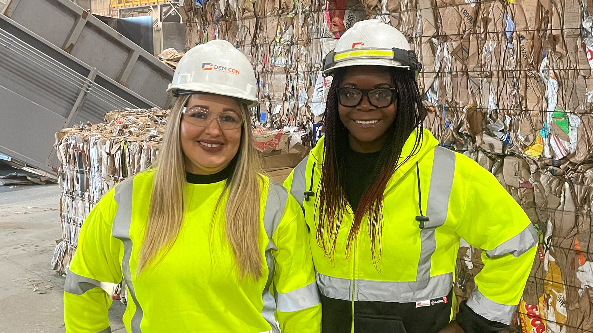 Close up of Dem-Con employees poses for the camera with a Material Recycling Facility bales of cardboard behind them